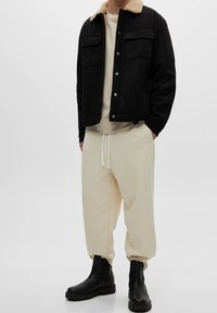 Sort ruskindjakke med en cremefarvet faux fur-krave, beige sweatshirt og løse beige sweatpants, suppleret med sorte ankelstøvler.