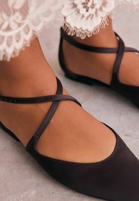 Ballerines noires à lanières croisées, avec une finition mate lisse, un design à bout pointu et un petit talon.