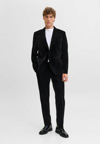 Juodas aksominis švarkas su notošiais atlapais, derinamas su tokio pat spalvos kelnėmis ir po apačia dėvima balta marškinėlių. Juodi odiniai batai užbaigia aprangą.