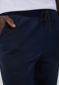 Marinblå joggingbyxor i ett mjukt tyg, med ett elastiskt midjeband och snörning, samt sidofickor.