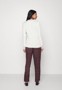 Camisola de mangas compridas em creme com detalhes em renda nos punhos, combinada com calças padrão em marrom. As calças apresentam um estampado geométrico e um corte reto.