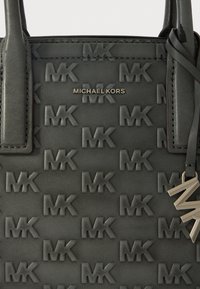 Czarna skórzana torebka z wytłoczonym wzorem logo "MK", metalowymi elementami w kolorze srebrnym oraz wiszącą zawieszką z inicjałami marki.