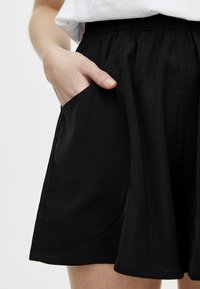 Sort shorts lavet af letvægtsstof, med elastisk talje og sidelommer med buede sømme. Glat tekstur, knælængde.