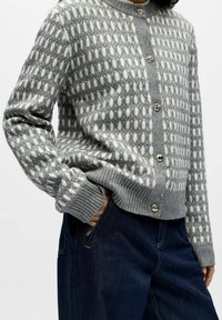 Szary i biały sweter we wzory z prążkowanym dołem i mankietami, z okrągłymi guzikami z przodu do zapięcia.