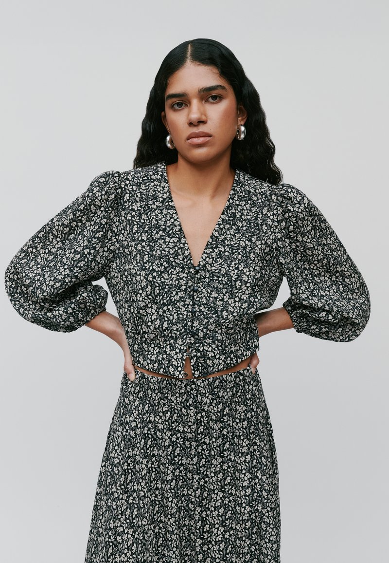 Svart blomstret crop-top med puffermer, teksturert stoff og dyp V-hals, med knapplukking foran og matchende mønstret skjørt.