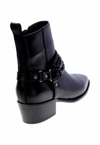Stivale alla caviglia in pelle nera con un tacco spesso, caratterizzato da una catena decorativa e dettagli con fibbia attorno alla caviglia. Texture liscia, punta rotonda.