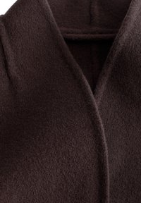 Manteau en laine marron foncé avec un large col et une surface douce et texturée visible en gros plan.