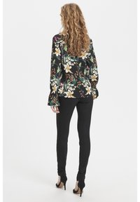 Svart blommig skjorta med långa ärmar som har vita och gula blommor, i kombination med svarta tajta byxor och svarta högklackade skor.