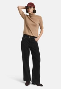 Pull à col montant beige à manches courtes, jeans noirs à coupe large, ceinture noire, casquette bordeaux, bottines brunes. Tenue simple et décontractée.