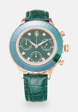 Orologio rotondo con cinturino in pelle verde texturizzata. Il quadrante presenta uno sfondo verde scuro, dettagli in cristallo e tre sub-quadranti. Hardware color oro.