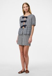 Top a maniche corte a righe con tre fiocchi frontali. Abbinato a pantaloni corti a righe coordinati. Entrambi in blu navy e bianco. Texture liscia e vestibilità rilassata.
