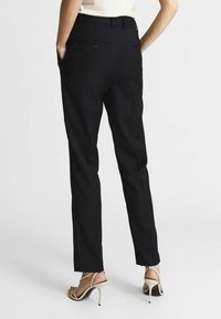 Pantaloni neri su misura con design a gamba dritta, dotati di due tasche posteriori con bottoni e una texture di tessuto liscia.