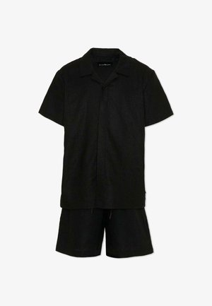 Chemise noire à manches courtes avec col, associée à un short noir à cordon, présentée sur un fond blanc.