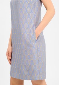 Robe sans manches de couleur bleu clair avec un motif de feuilles dorées. Dotée de poches latérales et d'une coupe droite. Texture lisse avec un léger éclat.