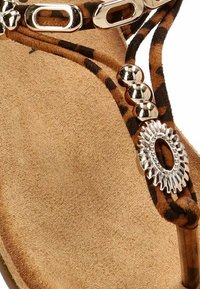 Sandal de tacón de ante marrón con tiras de estampado animal, acentos metálicos, cuentas esféricas y un adorno decorativo plateado.