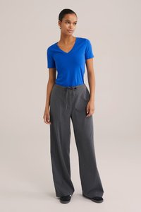 T-shirt bleu à manches courtes en V associé à un pantalon gris taille haute à jambes larges avec un design texturé à rayures fines et un cordon de serrage ajustable.