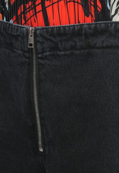 Pantaloni din denim negru cu închidere frontală cu fermoar, având o textură netedă și talie structurată, completată de un top viu colorat roșu cu model deasupra.