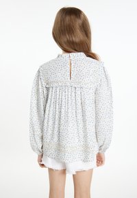 Lyseblå blomsterbluse med rynket udskæring og ærmer. Bagsiden har en nøglehulåbning og samlet stofdetalje.