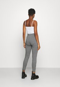 Czarno-białe legginsy w wzór houndstooth z wysokim stanem, połączone z białą koszulą na ramiączkach i czarnymi botkami za kostkę. Gładki materiał, dopasowany krój.