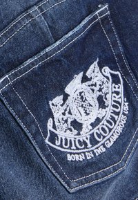 Τσέπη από σκούρο μπλε τζιν με λευκό κεντημένο λογότυπο "JUICY COUTURE" και σχέδιο με υφή. Λεπτομέρεια με μία ραφή.