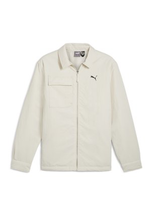 Kreemvalge jakk, millel on lukuga eesmine osa, terav krae ja pikad varrukad. Funktsioonide seas on üks rinnatasku ja must logoaktsent rinnas.