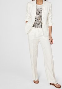 Biały zestaw składający się z lnianej marynarki i spodni, z koszulką w panterkę. Marynarka ma jeden guzik, a spodnie mają prosty krój nogawki.