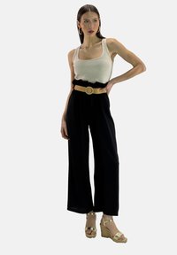 Zwarte wijde broek met een volants tailleband, gecombineerd met een aansluitend crèmekleurig tanktop en gouden sleehakken. Heeft een textuurriem van stro.