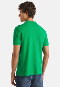 Zelené polo tričko vyrobené z bavlny, s klasickým límečkem a krátkými rukávy, hladkou texturou a rovním lemem. Nošeno s tmavými džíny.