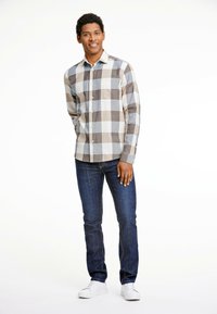 Geruite shirt in grijs en beige met een button-down kraag, gecombineerd met donkerblauwe jeans en witte sneakers. Shirt heeft een borstzak.