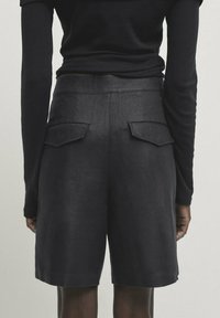 Shorts en lin noir avec une coupe ajustée. Le dos présente deux poches à rabat, une texture lisse et une taille mi-haute. Design simple et épuré.