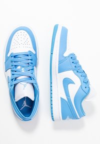 Ett par blå och vita lågskor med snörning, synlig Nike swoosh och Air Jordan-logotyp på tungan och hälen.