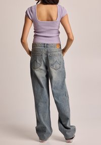 Fialový pruhovaný top se čtvercovým výstřihem vzadu, spárovaný se světle modrými kalhotami s širokými nohavicemi, které mají zadní kapsy a béžový kožený štítek.