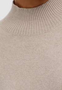 Maglione beige lavorato a maglia con colletto alto a coste, texture morbida e design senza cuciture. Semplice, classico e versatile per gli strati.