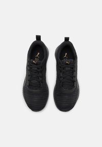 Zapatillas deportivas negras con parte superior de tela texturada, cordones planos, tira de agarre y un sutil acento de logo dorado. Suela de goma redondeada para mayor tracción.