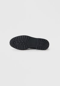 Suela de zapato de goma negra con surcos profundos, presenta una superficie texturizada y una sección central lisa. Diseñada para tracción y estabilidad.