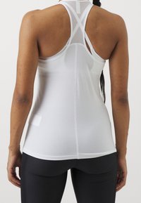 Top in rete bianco con design a racerback, caratterizzato da una superficie texturizzata e cuciture senza soluzione di continuità. Abbinato a leggings neri aderenti.