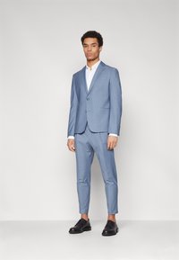 Ljusblå skräddarsydd kostym med enknappl Blazer och slim-fit byxor. Vit skjorta under, tillsammans med svarta snörskor.
