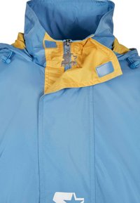 Giacca a vento light blue e gialla con colletto alto, chiusura a zip, toggle regolabili e logo sul davanti. Texture liscia.