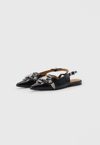 Black leather slingback shoes with pointed toes, decorative silver hardware, and a low heel. The interior features a tan lining.