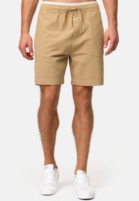 Pantalones cortos de algodón color beige con cintura elástica y cordón. Con dobladillos y un ajuste relajado. Llevados con zapatillas blancas.