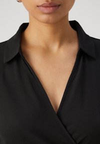 Μαύρη μπλούζα με κολάρο σε σχήμα V και διακριτική υφή. Κοντινή άποψη της περιοχής του κολάρου και του λαιμού.