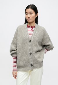 Hall hallitud kootud kardigan v-kaelusega, ülepõlvevarrukatega, kahe eesmise tasku ja mustade nuppudega. Sellel on soonikkoes mansetid ja palmikmustritega kudum.