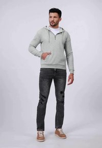 Svetlošedá mikina na zips vyrobená z mäkkého materiálu s klokankou. V kombinácii s čiernymi roztrhnutými úzkymi džínsami a pieskovými teniskami.
