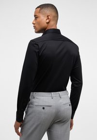 Zwarte lange mouwen shirt met een klassieke kraag; gladde textuur. Grijze tailored broek met dubbele achterzakken en knoopaccenten.