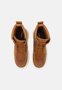 Botas de cuero marrón hasta el tobillo con cordones naranjas, costuras texturizadas y una suela de goma color crema, con una lengüeta en el collar.