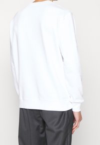 Sudadera blanca con cuello redondo, mangas largas, puños y dobladillo acanalados. Tejido de algodón suave con una textura lisa, sin patrones ni acentos.