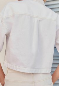 Giacca di denim bianca cropped con cuciture sottili e una vestibilità rilassata, abbinata a pantaloni chiari a vita alta.