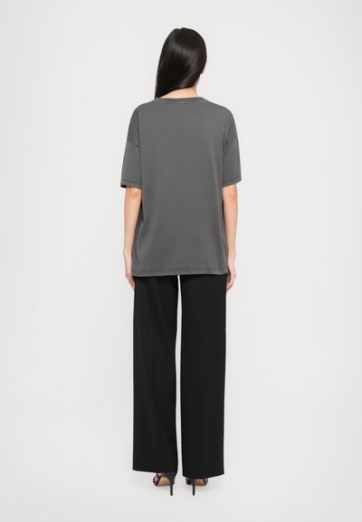 Tricou oversized gri cu mâneci scurte și guler rotund, asortat cu pantaloni largi negri, afișat dintr-o perspectivă din spate.