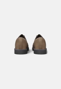 Hnědé kožené boty s kulatou špičkou, plochou černou podrážkou a viditelnými švy. Design je čistý a minimalistický.