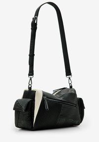 Borsa in bianco e nero realizzata con materiali testurizzati, caratterizzata da rigature verticali e orizzontali, cerniere argentate e una tracolla regolabile.